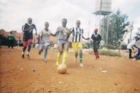 Children playing football on a dirt pitch in Kibera
